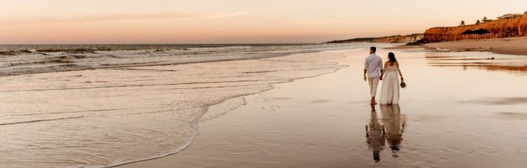 A bride and groom walking on a beach together.