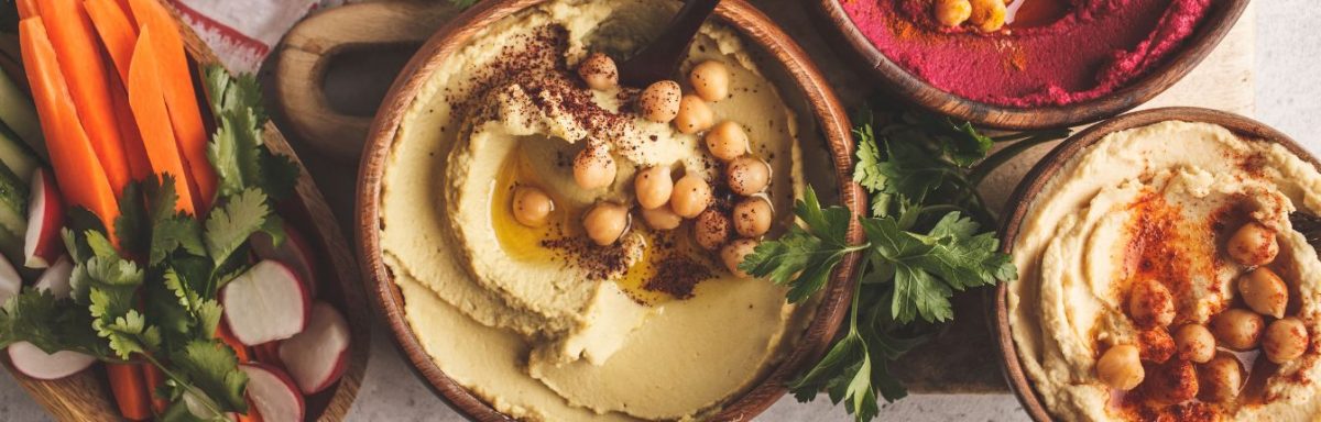 Bowls of hummus with chickpeas on top, and carrot sticks on the side.