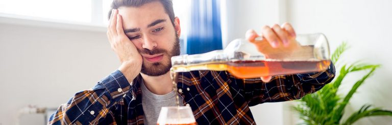 A man pouring himself a glass of whisky. He looks very tired.